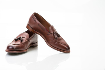 Footwear Concepts. Pair of Traditional Formal Stylish Brown Pebble Grain Tassel Loafer Shoes On White Reflective Surface.