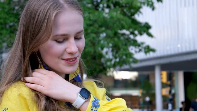 straighten hair with hands long dangling earrings in blue and yellow embroidery blue flowers. girl is wearing an embroidered shirt, national Ukrainian Slavicclothes, a yellow shirt. 