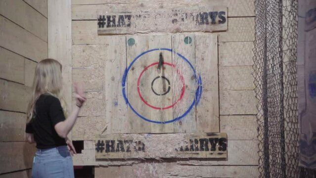 Young blonde Female throwing an axe at a target from above her head