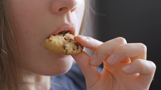 Close up view, young caucasian woman eating chocolate chip cookie