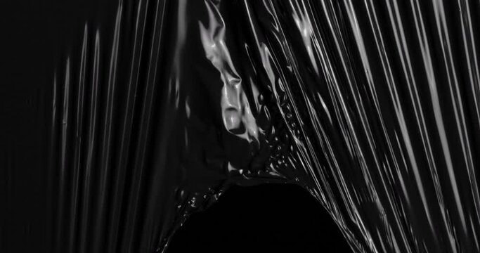 Immerse yourself in an extraordinary tactile experience as stretched plastic film cascades against a backdrop of deepest black, unfolding like a sculptural masterpiece of rumpled cellophane wrap.
