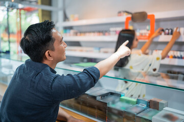 male customer pointing on the liquid arranged at the store shelf to guiding the seller