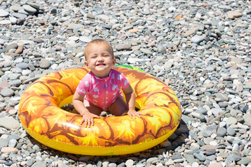 little happy smiling girl with giant rubber swimming ring on the beach by the sea