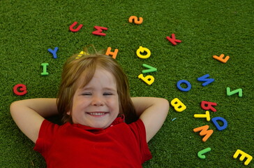 A preschooler plays with English letters. Learning the alphabet in kindergarten. The boy laughs - a fun lesson on the grass Copy Space