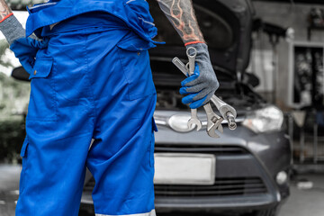 Close up hands of a male car mechanic from behind holding wranches with car in background