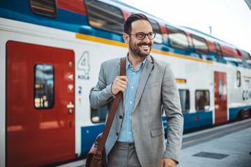 Photo of a smiling businessman at train station.  Confident professional is wearing suit. He is...