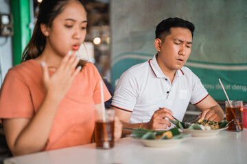 handsome man with a spicy expression eating pecel with Asian woman at a traditional food stall