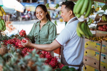 female customer smiling while helped by the male employee to choosing the dragon fruits at the...