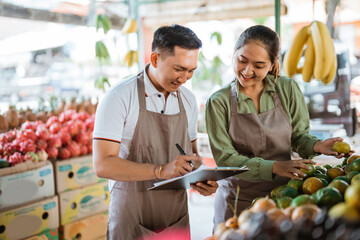 female fruit seller checking the oranges while looking at the clipboard that holded by the male...