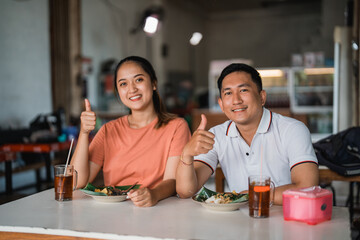 Asian couple shows thumbs up while eating together at a pecel food stall