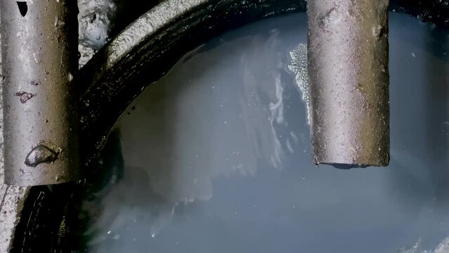 Black chemical wastewater pouring on the storage tank coming out from pipe from industrial processes. Hazardous and toxic waste water - WWTP Wastewater Treatment Procedure