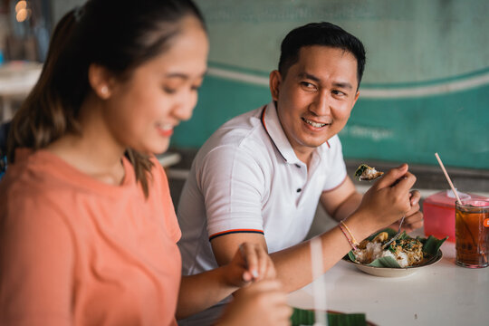 handsome man looks at beautiful woman while eating lotek at a table in a traditional food stall