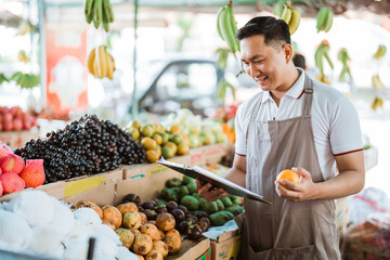 male fruit seller holding the mandarin fruit while checking the fruit list at the background
