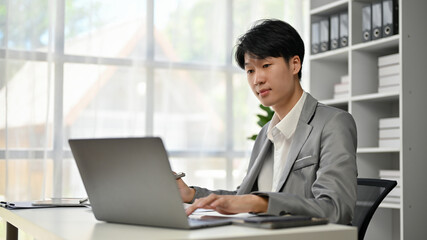 A handsome and smart Asian businessman focuses on his business work on his laptop