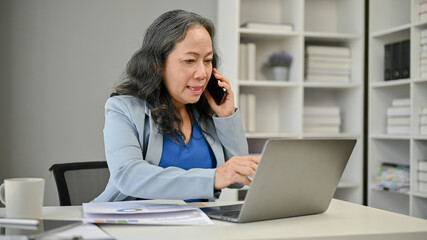 A professional Asian senior businesswoman is negotiating business over the phone