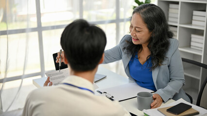 A kind mature Asian businesswoman explaining work to a young male worker