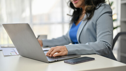 A professional Asian senior businesswoman using her laptop at her desk.