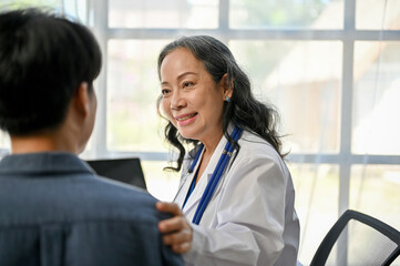 A kind Asian senior doctor touching a patient's shoulder to comfort him during a medical checkup
