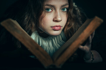 Portrait of a frightened young woman with a book on a dark background. - 622584823