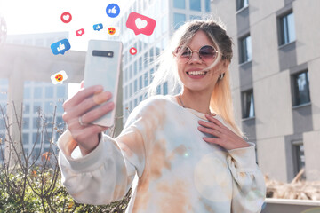 A young beautiful girl blogger takes selfies among the cityscape on a sunny day.
