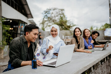 Asian male and female college students using a laptop computer in an outdoor coworking space