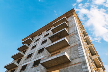 Unfinished residential reinforced concrete building apartments under construction against the blue sky