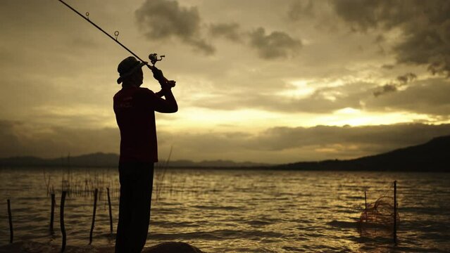 Silhouette of a fisherman with a fishing pole at sunset and enjoying hobby, catch of fish