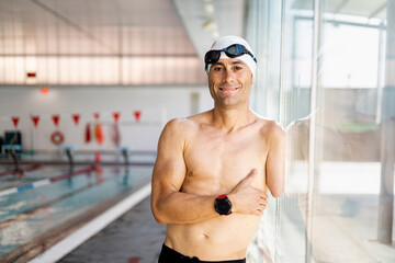 Portrait of an adult swimmer with an amputated arm is posing on a glass of an indoor pool while...