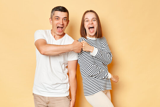Excited laughing young couple friends man woman in casual clothing isolated over beige background making fist bump deal sreaming with happiness celebrating good idea.