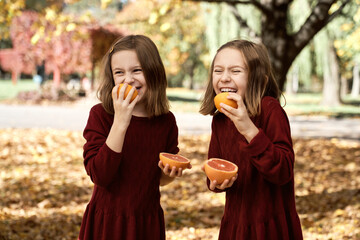 Child siblings standing in the woods and having fun while eating citrus fruits