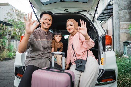 happy asian muslim family with kid sitting in the car trunk with suitcase showing thumb up