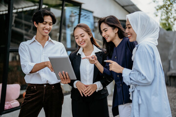 Group of cheerful young businesspeople using a tablet work together on a new project while standing...