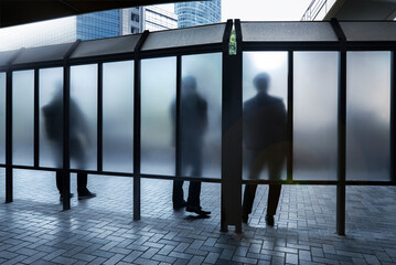 City scene of people stood behind frosted glass at urban shelter or bus stop