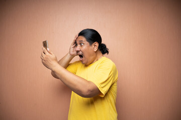 old asian man wearing yellow tshirt holding handphone and using it to texting or video call with each other in plain background isolated