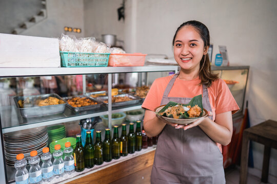 Asian waitress shows a plate of delicious Asian food pecel rice at a food stall