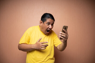 old asian man wearing yellow tshirt holding handphone and using it to texting or video call with...
