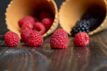 Red ripe raspberries with waffle cups on a black table