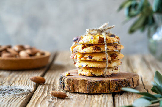 Florence cookies or fiorentine biscuits with almonds on wooden standl, almonds on plate, olive tree branch over wooden table with grey background