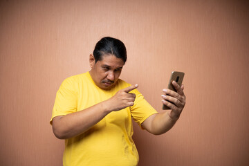 old asian man wearing yellow tshirt holding handphone and using it to video call with pointing...