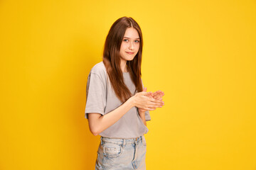 Portrait of young beautiful girl, student in casual clothes posing against yellow studio background. Smiling. Concept of human emotions, fashion, youth, lifestyle, female beauty, ad