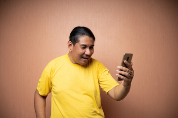 old asian man wearing yellow tshirt holding handphone and using it to texting or video call with each other in plain background isolated