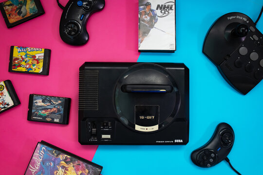 Sevastopol, Russia: July 11, 2023: Collection of retro video game sega mega drive and cartridges, gamepads, on a blue and pink background, top view. Sega has released the Mega Drive console in Japan