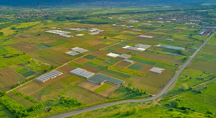 Fototapeta premium Green agricultural fields with various crops and greenhouses to protect plants from bright sunlight and hot weather in a garden plot. Panoramic top view from a drone