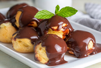 Delicious profiteroles with chocolate and white plate. Selective focus image on light background.