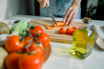 Crop anonymous housewife cutting carrot in kitchen while preparing healthy salad with tomatoes and herbs during cooking at home