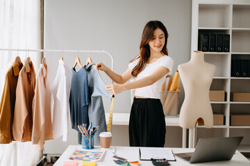 Asian young woman on desk in office of fashion designer and holds tablet, laptop and smartphone on white table