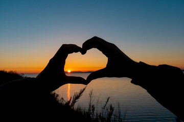 Hands of a couple in love in the shape of a heart while walking by the sea in the evening.