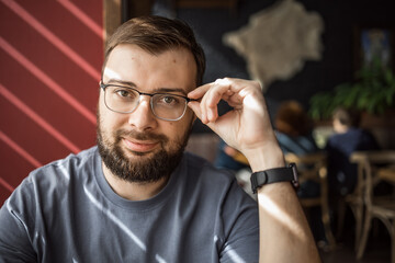 Handsome, fashionable man with glasses and a beard looking directly camera in a restaurant. Vision...
