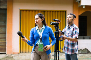 a female reporter in blue cardigan with green name tag hunting for news with a cameraman behind her