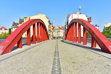 Part of the bridge with red metal semicircular supports, a road paved with stone and buildings in the background. Poland, Poznan, June 2022